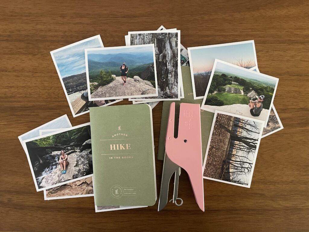 A bunch of 3-inch by 4-inch photos from a bunch of my different hikes spread around a Letterfolk Hike Passport and pink Ellepi stapler atop my wooden desk.