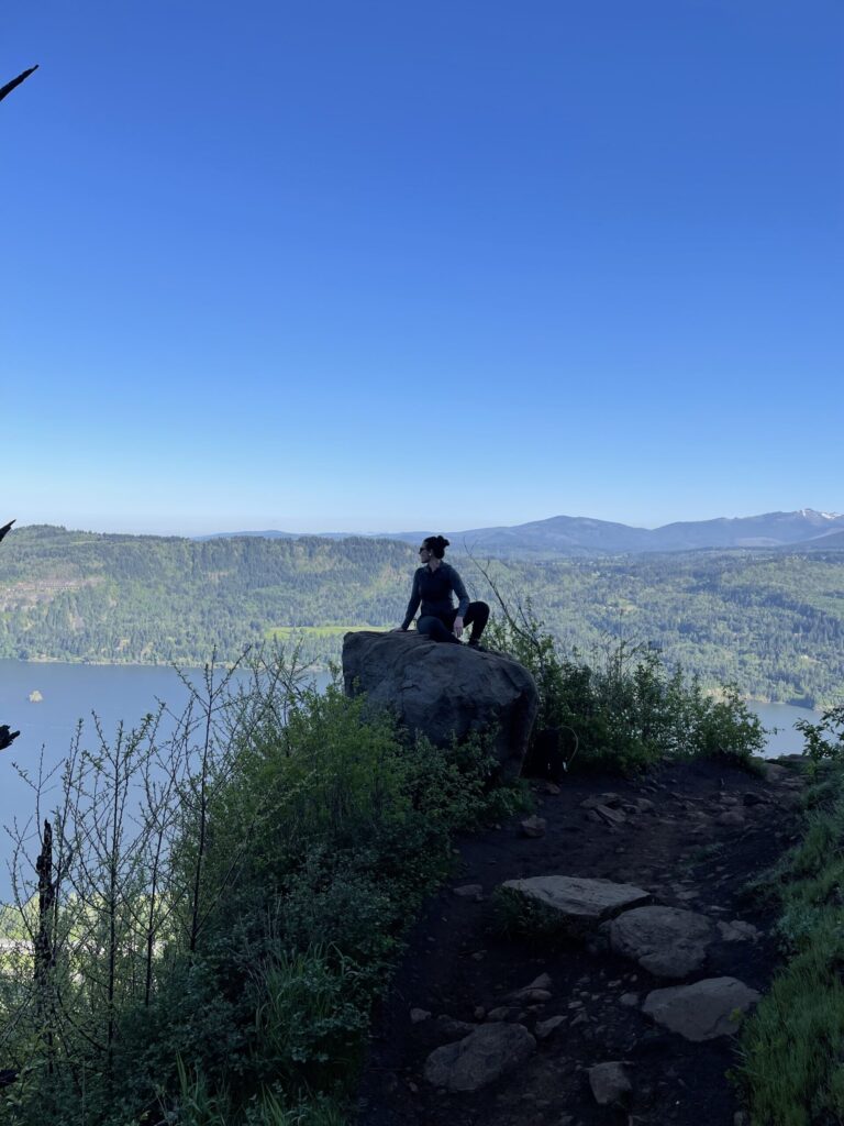 A photo of me on a boulder in May 2022, with the Columbia River in the background.