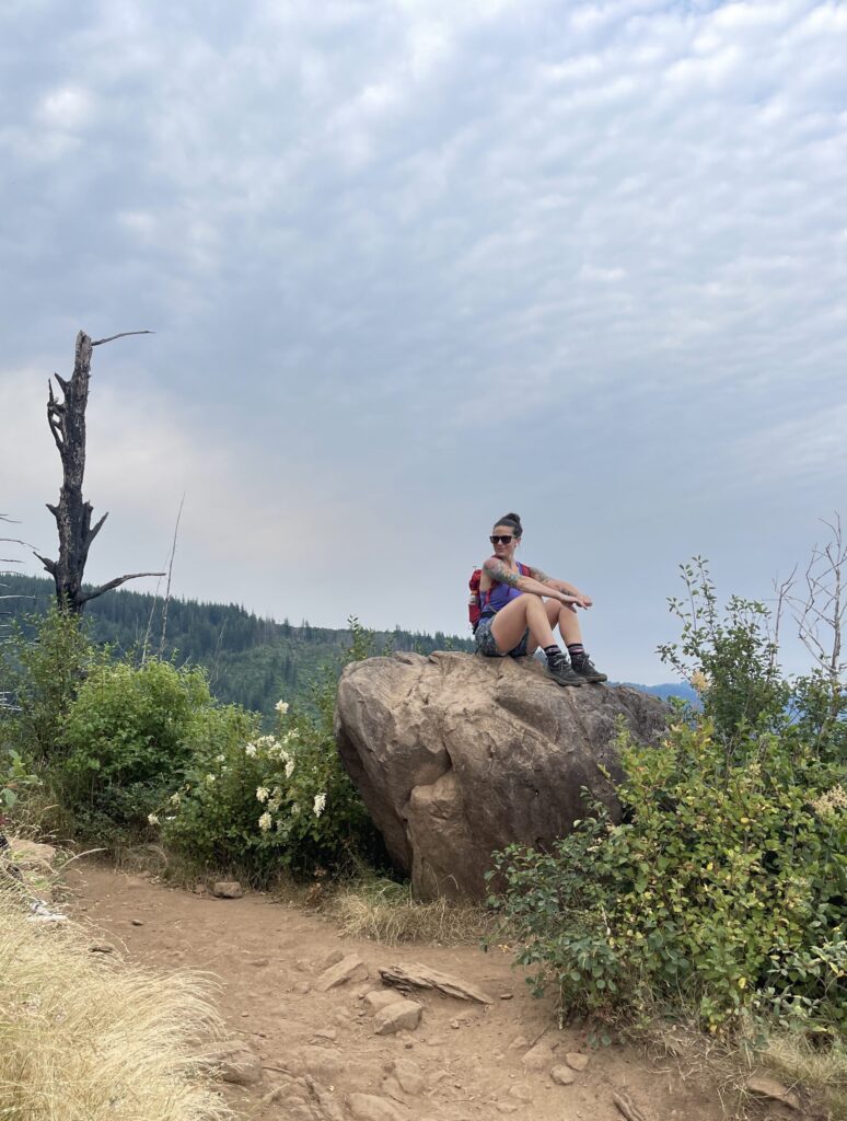 A photo of me on a boulder in July 2022, with the Columbia River in the background.