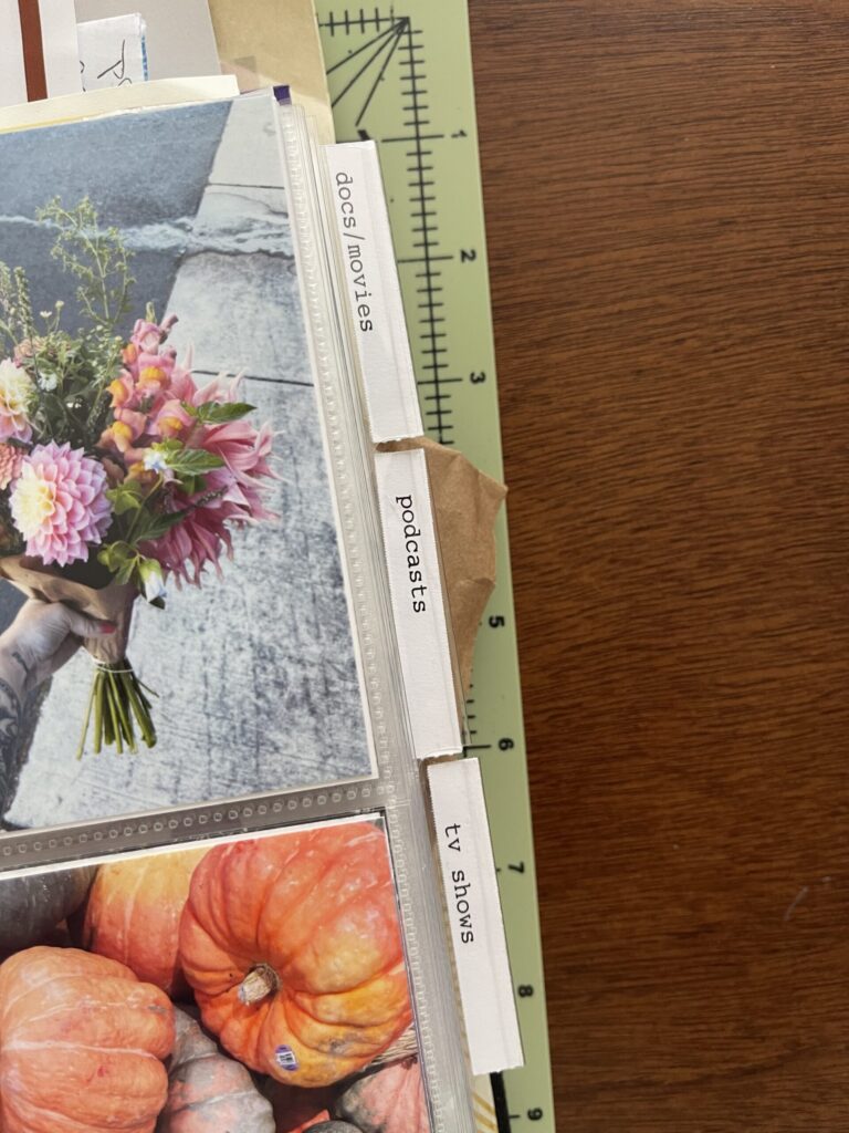 Close up of the edges of the page protectors, showing the tabs holding labels that mark each category of media I consumed in 2024: docs/movies, podcasts, and tv shows. 