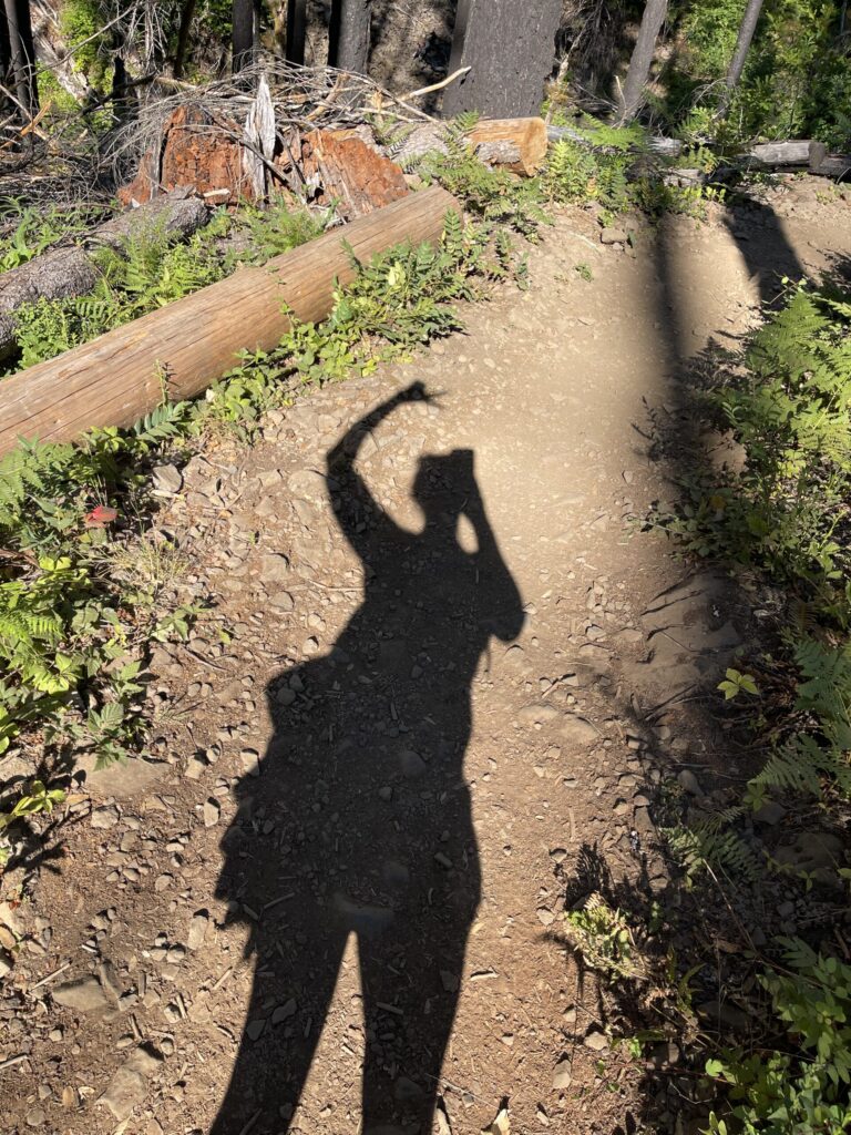 My shadow on the trail, with one hand throwing up a peace sign above my head.