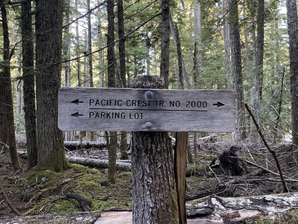 A sign in the forest along the trail noting which directions the Pacific Crest Trail run, and which way to go to get back to the parking lot. 