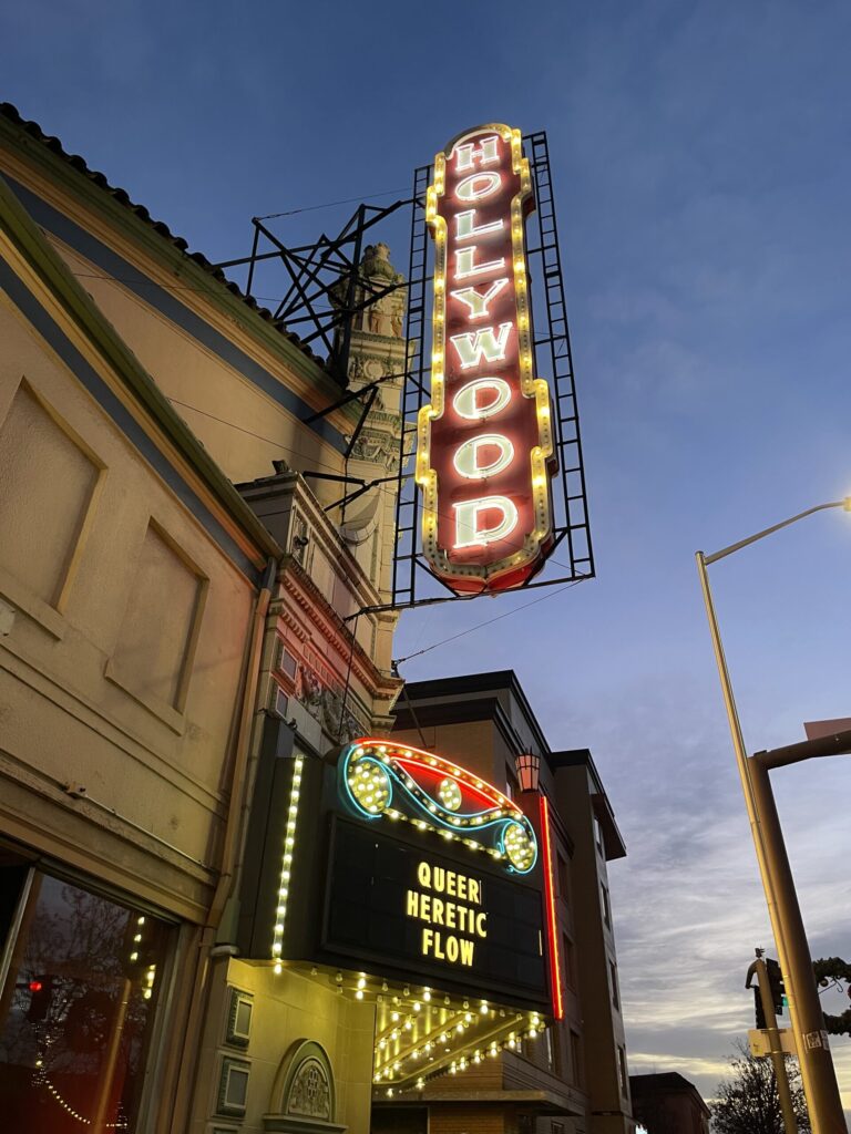 The iconic Hollywood Theater marquee in Portland, OR, advertising then-current showings of the movies "Queer," "Heretic," and "Flow."