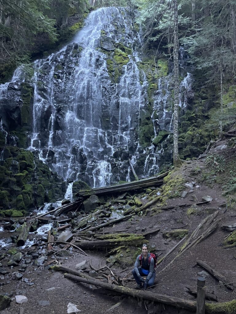 Me, tiny, crouching in front of Ramona Falls, an enormous fan waterfall in the Mount Hood National Forest. 