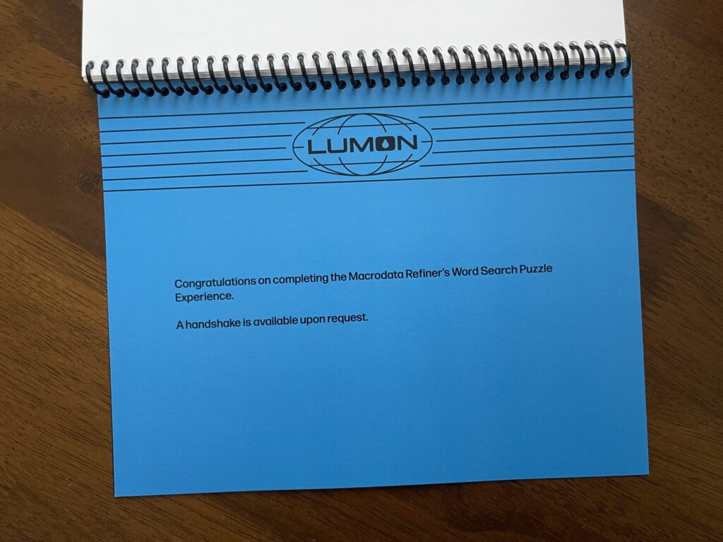 Bright, darker blue page featuring the Lumon letterhead and the words, "Congratulations on completing the Macrodata Refiner's Word Search Puzzle Experience. A handshake is available upon request."