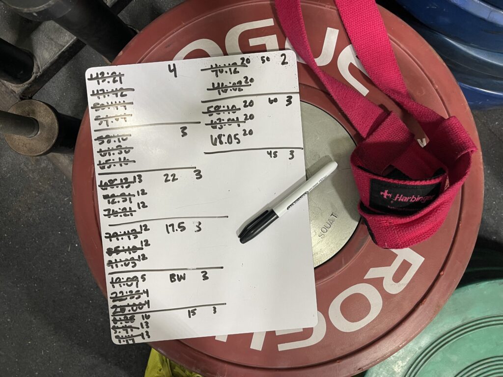 A mini whiteboard with clock times written down and scratched out, resting on top of a weightlifting bumper plate. 