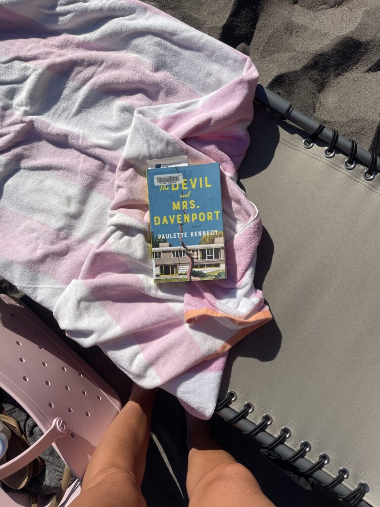 Overhead view of my new outdoor bag, and my fancy tanning lounge chair with beach towels and library book set up in the sand on the bank of a river. 