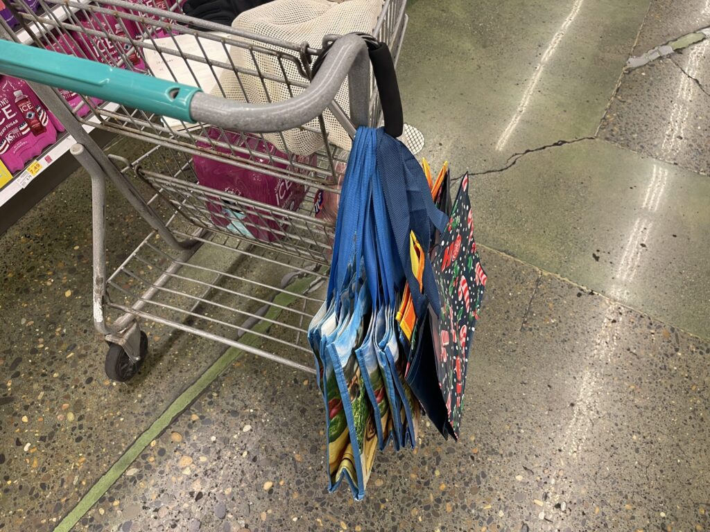 My collection of reusable grocery bags clipped to a shopping cart with a large carabiner. 