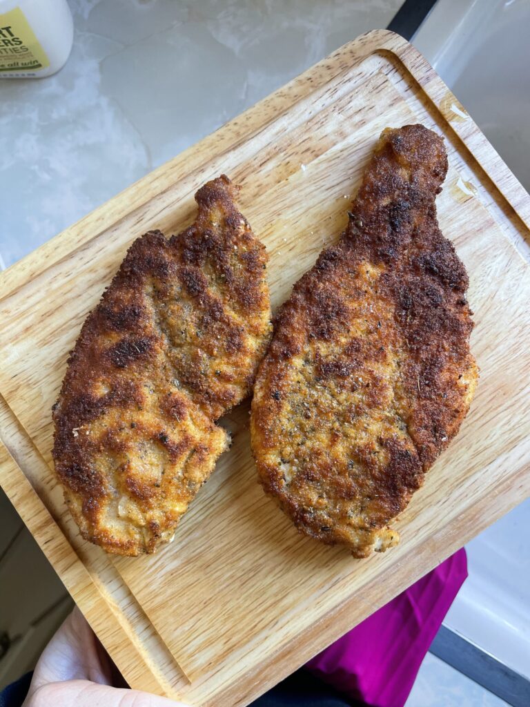 Two perfectly golden breaded chicken breast on a cutting board. 
