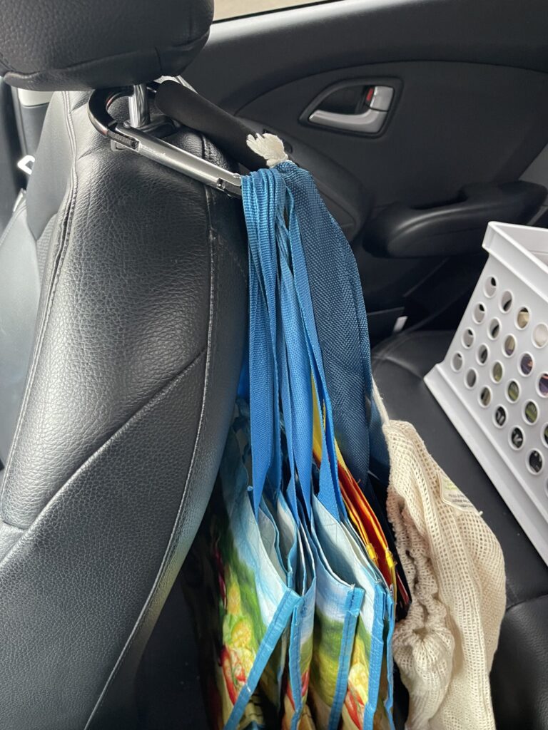 My collection of reusable grocery bags clipped to the passenger seat headrest in my car with a large carabiner. 