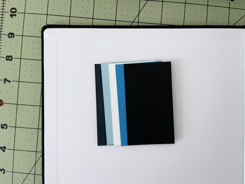 Paper samples of the colors I selected, arranged on a white background. The colors are: a deep navy blue, a lighter blue, white, a brighter-darker blue, black.