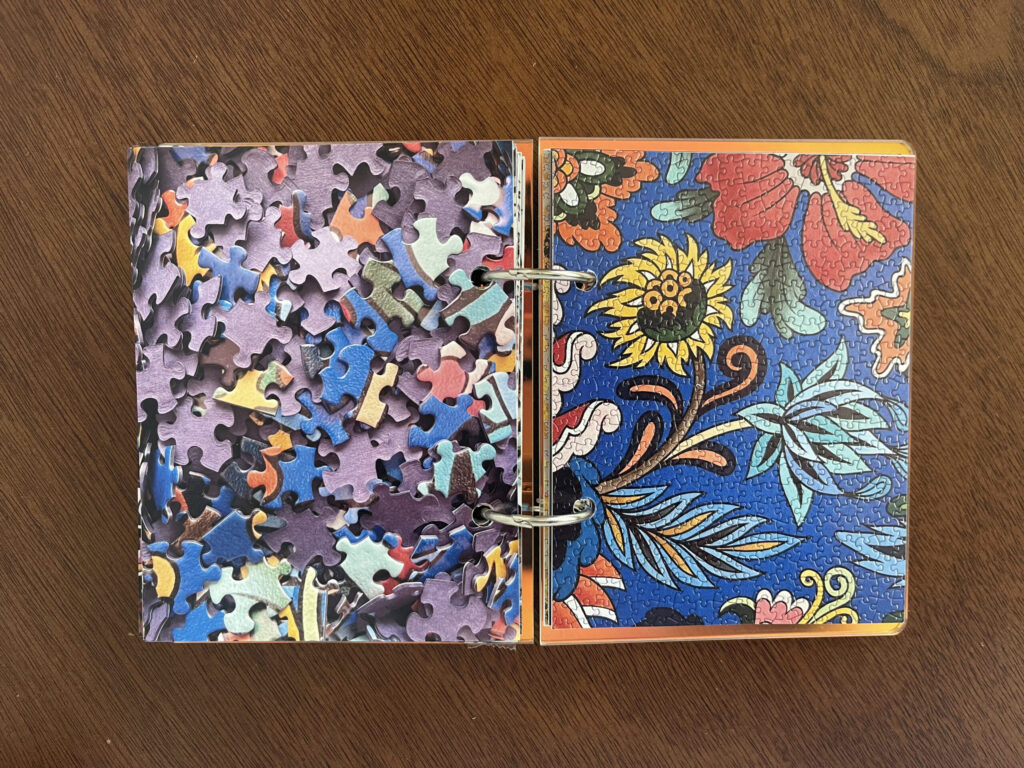 Spread #1. The left-hand page is a photo of the puzzle's unpuzzled pieces. The right-hand page is a photo of the completed puzzle of various brightly colored flowers painted on a blue wall.
