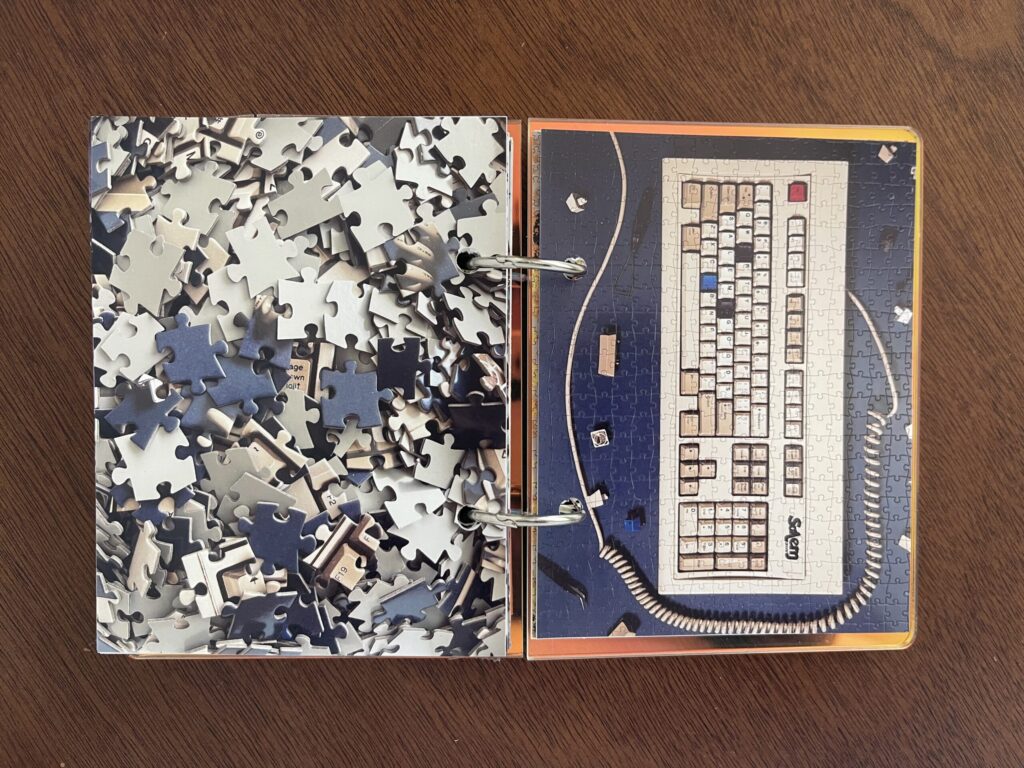 Spread #3. The left-hand page is a photo of the puzzle's unpuzzled pieces. The right-hand page is a photo of the completed puzzle of a photo of an old computer keyboard with a coil cord. 