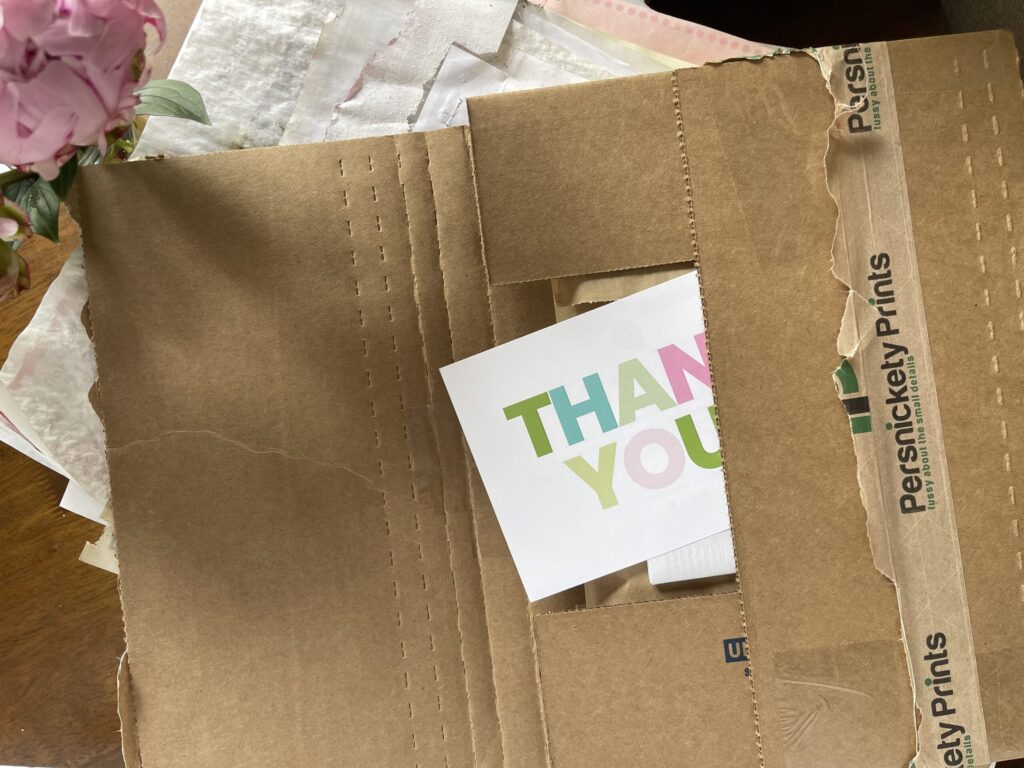 A cardboard mailer full of photos printed by Persnickety Prints open on my dining table, with a colorful "thank you" card peeking out. 