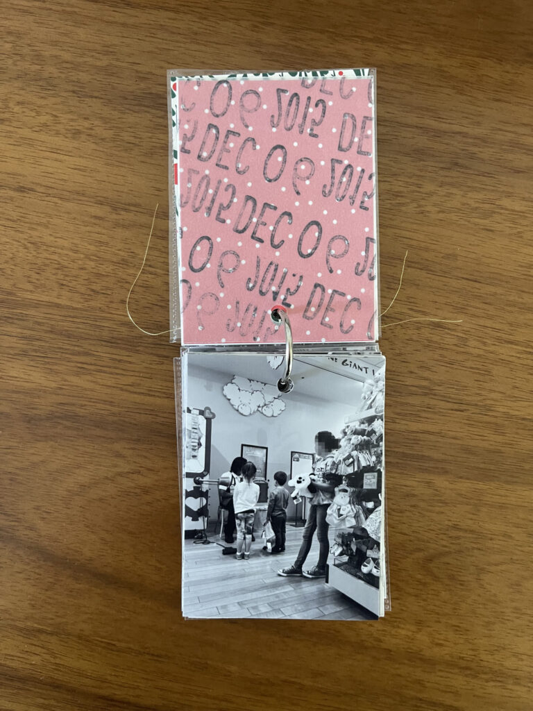 2015: the vellum page stamped with the date is flipped over to reveal a black-and-white photo of three kids in line to have their stuffed animals stuffed by the Build-A-Bear employee. 