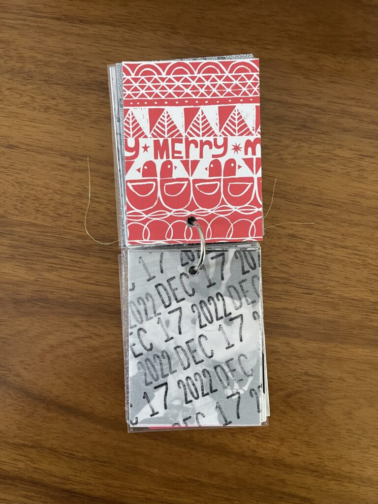 2022. The top page is a piece of patterned paper. The bottom page is a piece of vellum stamped repeatedly with the date. Beneath the vellum is a black-and-white photo from that year's visit. 