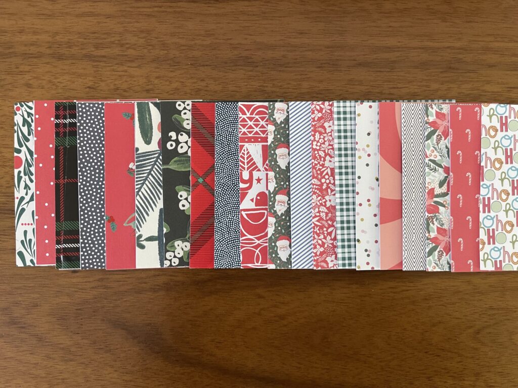 Various holiday-themed papers cut down to 3 inches by 4 inches and arranged in one long row, overlapping.