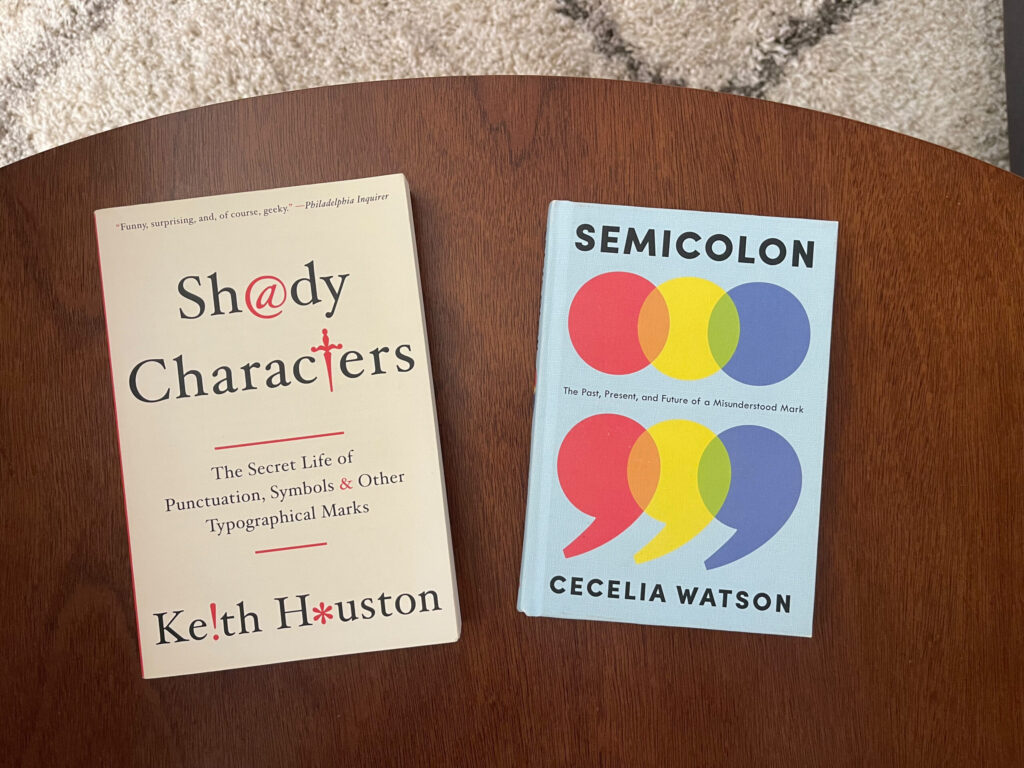 The books "Semicolon" and "Shady Characters" face up on a wooden table.